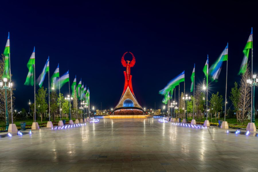 UZBEKISTAN, TASHKENT - MAY 5, 2023: Illuminated monument of independence in the form of a stele with a Humo bird, fountains and waving flags in the New Uzbekistan park at nighttime in spring.